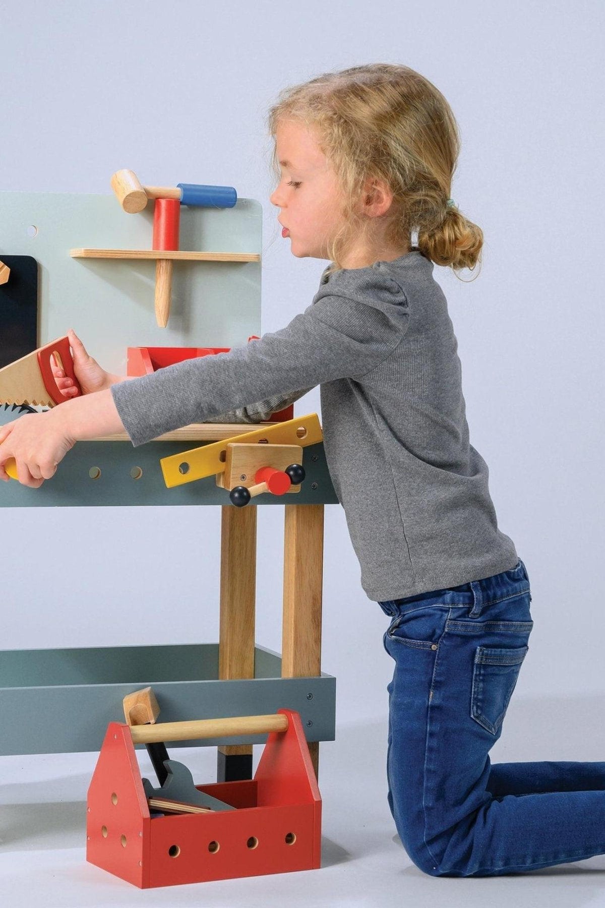 A child plays with Mentari Wooden Toys Carpenters Workshop, featuring colorful wooden tools and a workbench, encouraging creativity.