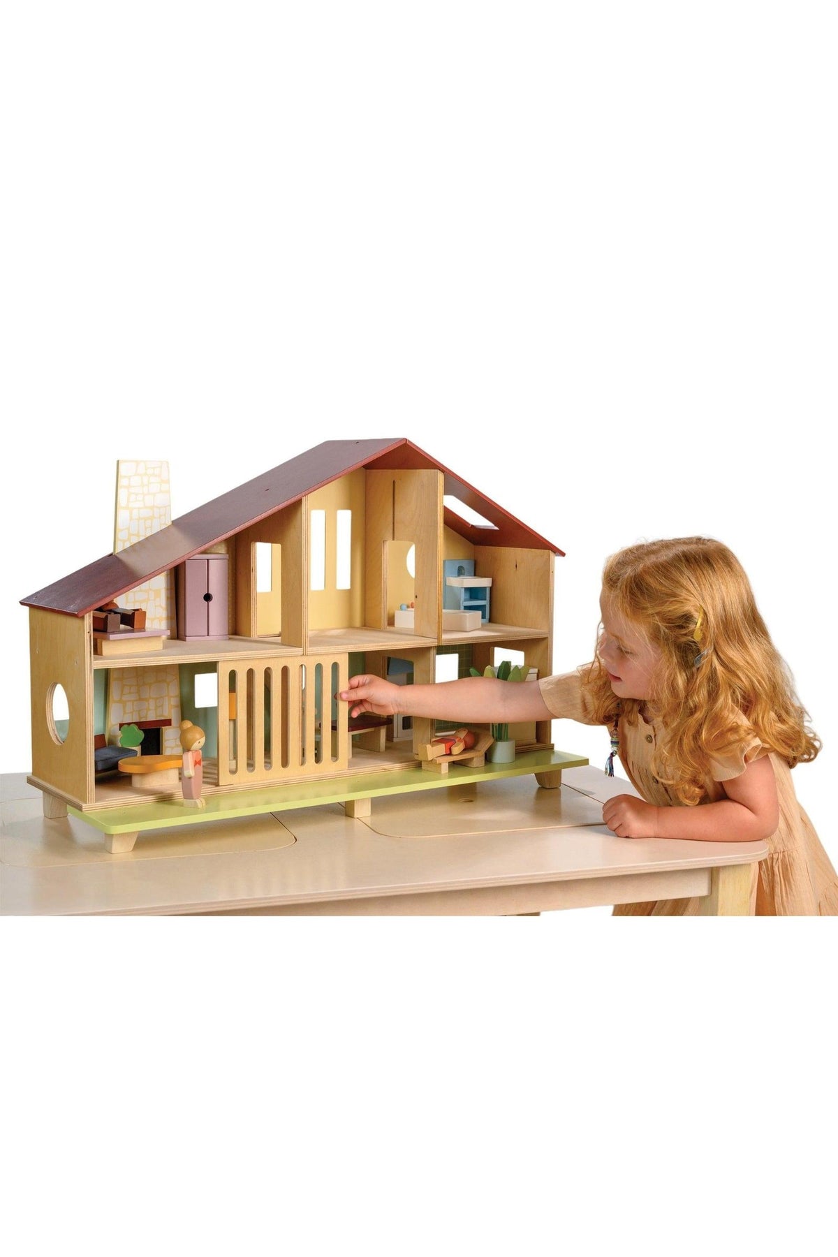 A child plays with a wooden dollhouse featuring open spaces and a red roof, showcasing modern design elements.