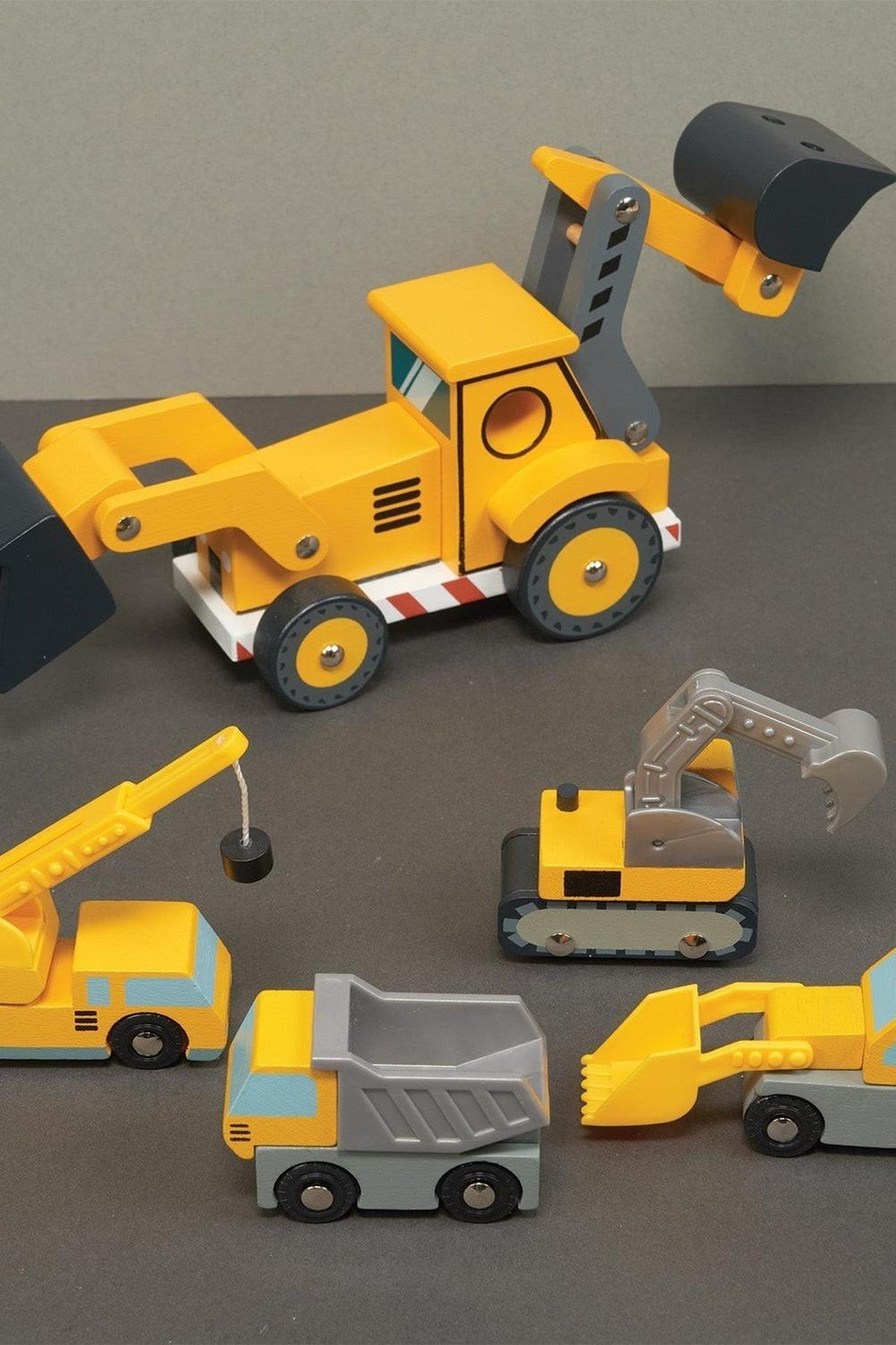 Wooden toy construction vehicles, including a backhoe, crane, dump truck, and excavator, in vibrant yellow.