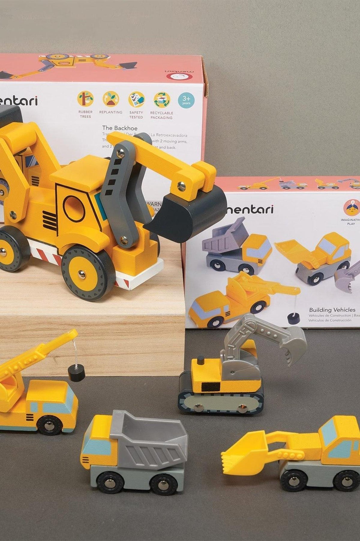 Yellow and gray wooden construction vehicles, including a backhoe and crane, are displayed with Mentari packaging.