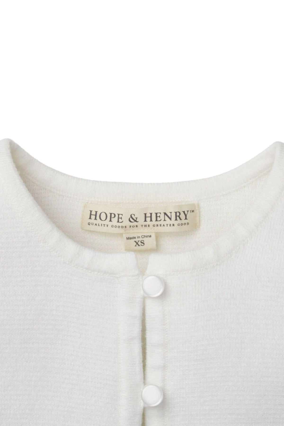 Close-up of a white Hope & Henry organic cotton cardigan featuring a button closure and soft texture, labeled XS.