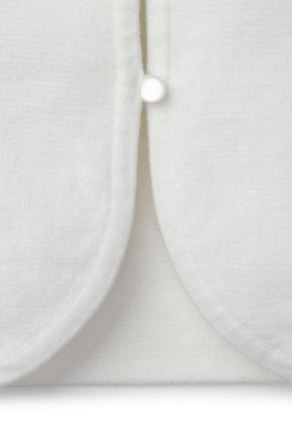 Close-up of a white organic cotton cardigan featuring a curved hem and a pearlized button closure.