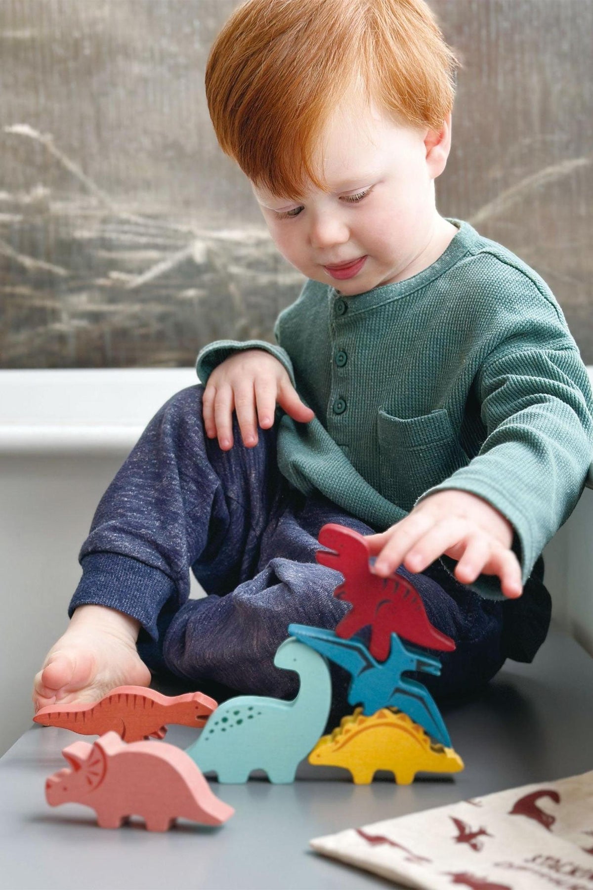 A child in a green shirt plays with colorful wooden dinosaur stacking toys on a gray surface.