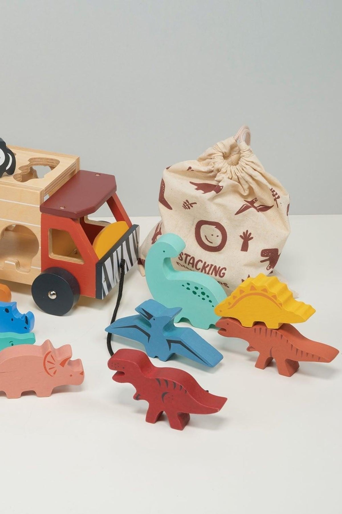 Colorful wooden dinosaurs and a safari truck are displayed with a drawstring bag labeled Stacking.
