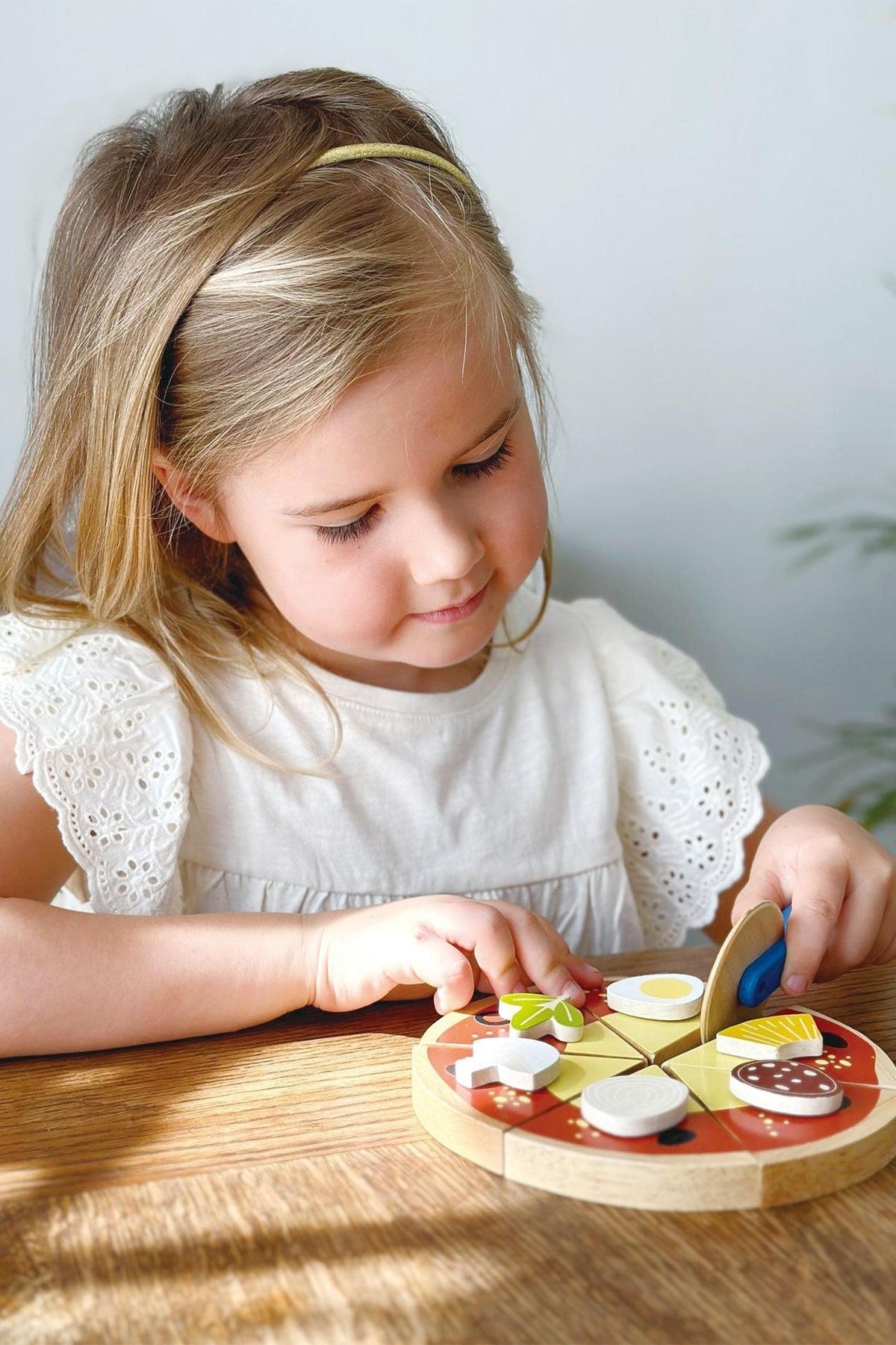 A child plays with a wooden pizza set, featuring colorful toppings, on a wooden table.