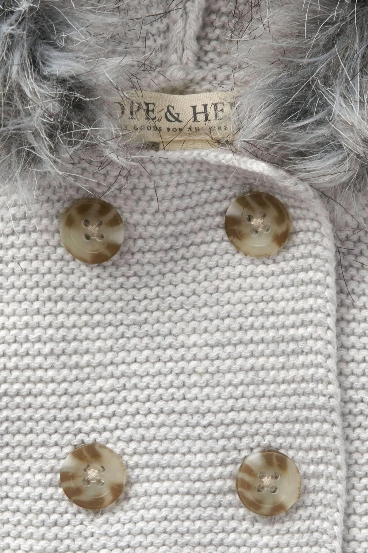 Close-up of a light gray knitted sweater featuring faux fur trim, with two decorative buttons and a Hope & Henry.
