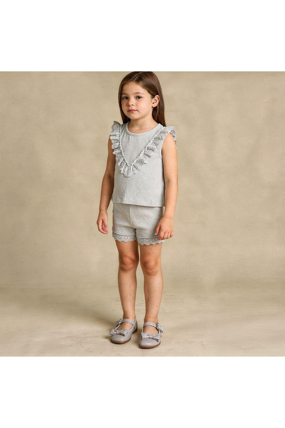 A young girl stands wearing an organic cotton gray ruffle top and matching shorts set, featuring delicate lace trim.