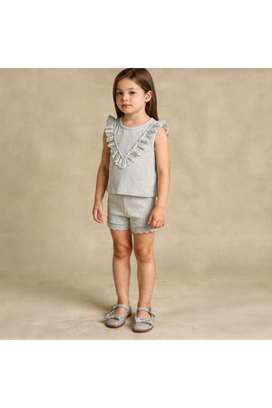 A young girl stands wearing an organic cotton gray ruffle top and matching shorts set, featuring delicate lace trim.