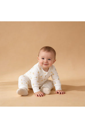A smiling baby sits on a soft, neutral background, wearing an organic cotton romper adorned with a lemon pattern.