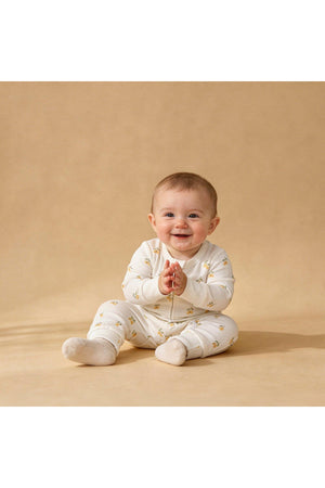 A smiling baby sits on a beige surface, wearing an organic cotton romper adorned with lemon patterns.