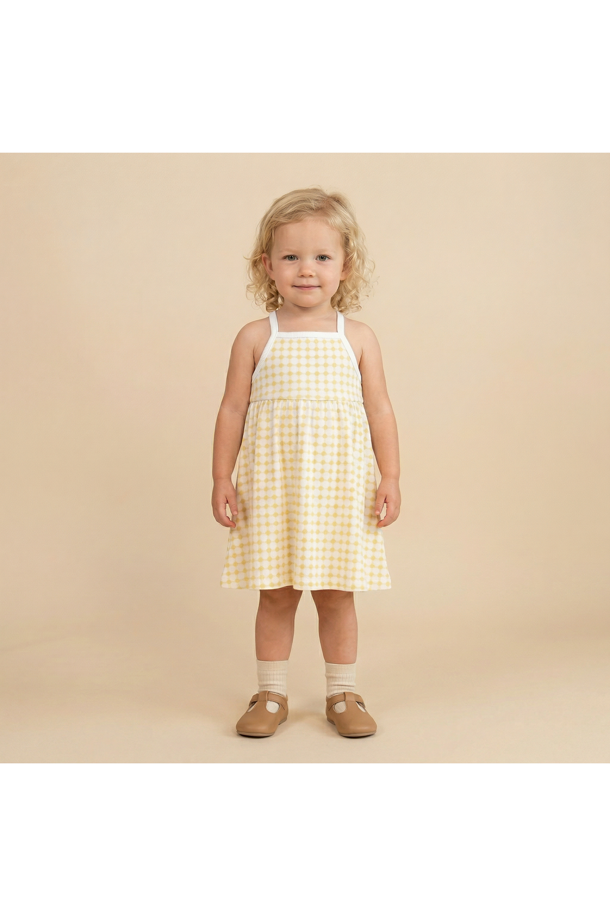 A young child stands smiling in a yellow and white gingham tie-back strap dress. The dress features a comfortable fit, perfect for warm days.