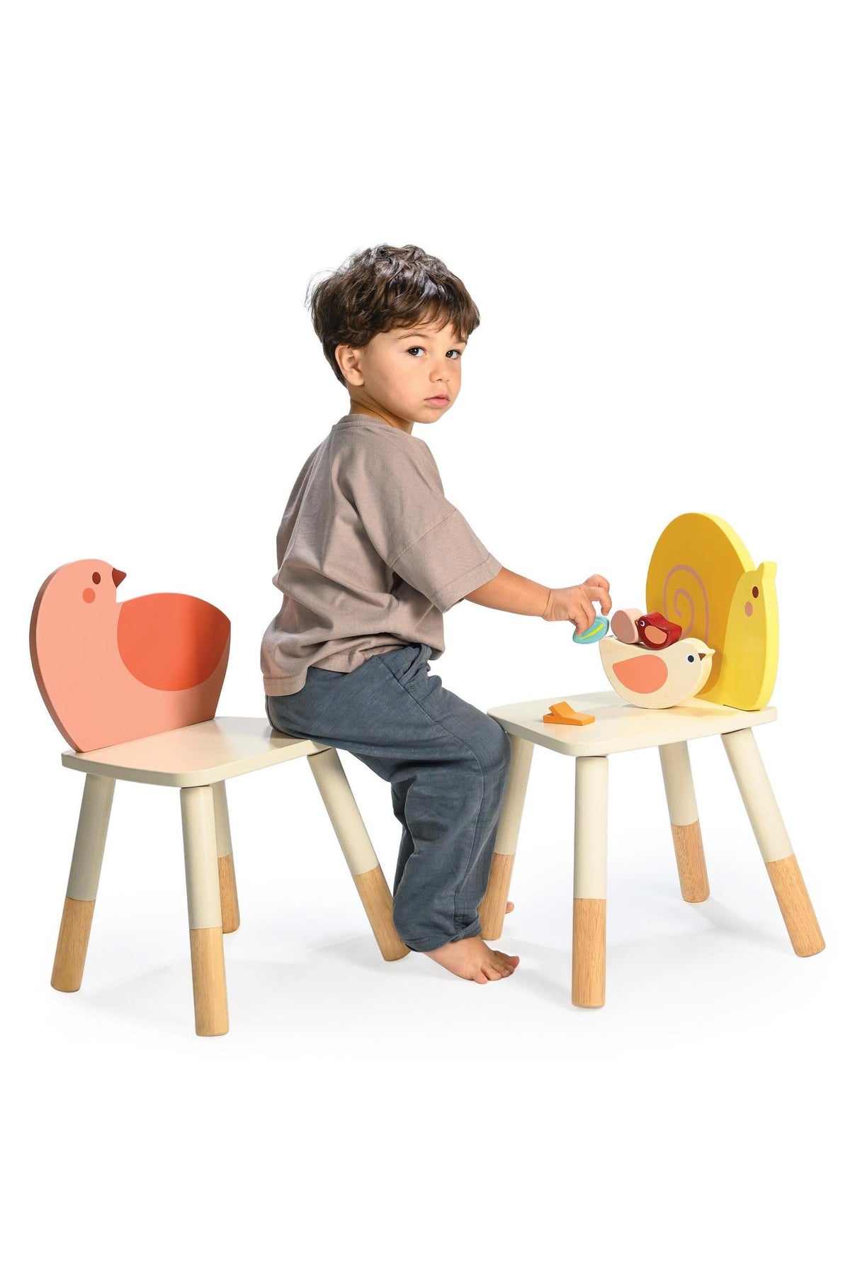 A child sits between two chairs with animal-themed backrests, one featuring a yellow snail and the other a bird.