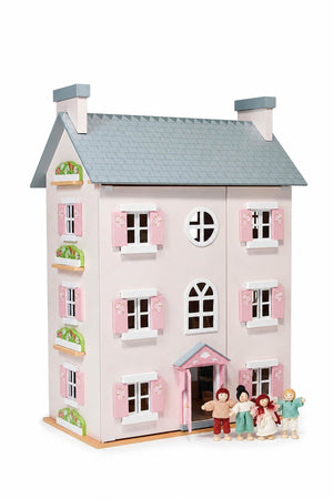 A charming wooden dollhouse with a pink and white exterior features flower-adorned shutters and a blue roof. The set includes five colorful doll figures, perfect for imaginative play.