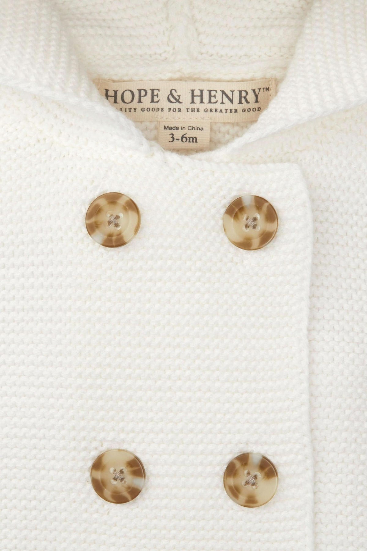 Close-up of a soft white seed stitch knit hooded sweater by Hope & Henry, featuring double-breasted buttons and a size.