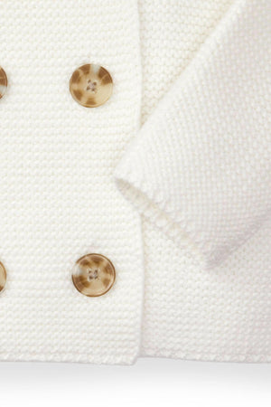 Close-up of a soft white seed stitch knit sweater featuring double-breasted buttons, crafted from organic cotton for added comfort.