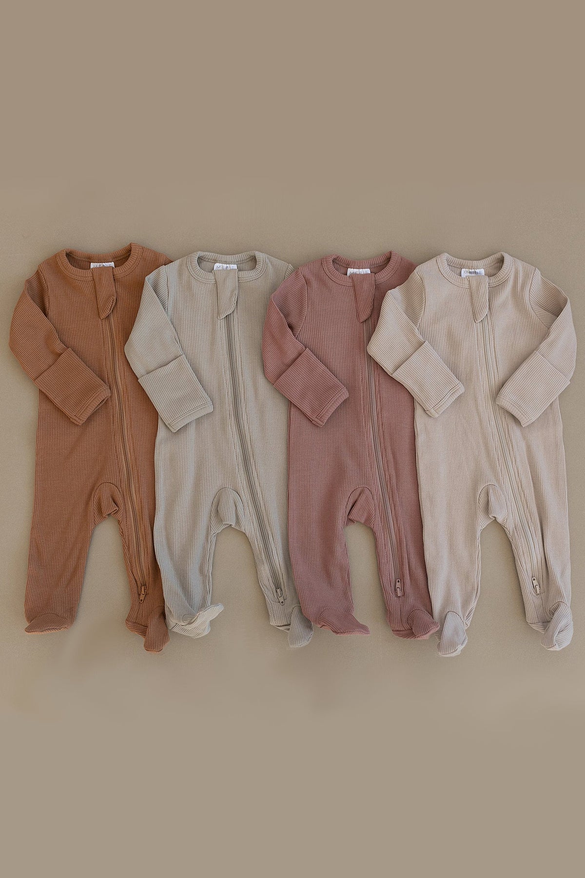 Four ribbed baby pajamas in earthy tones with zippers, displayed on a neutral background.