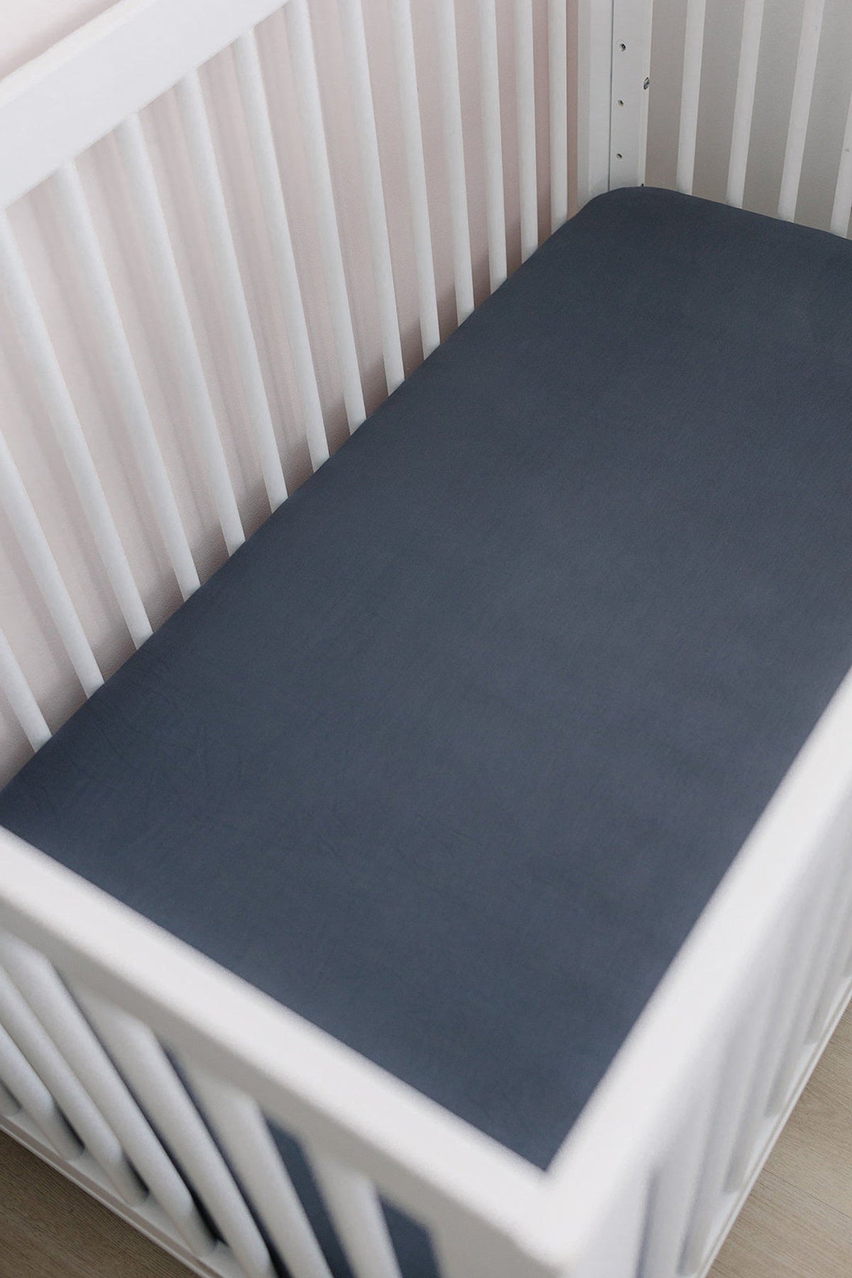 White crib with a charcoal stretch crib sheet, set against a light-colored wall. Made from soft bamboo fabric.