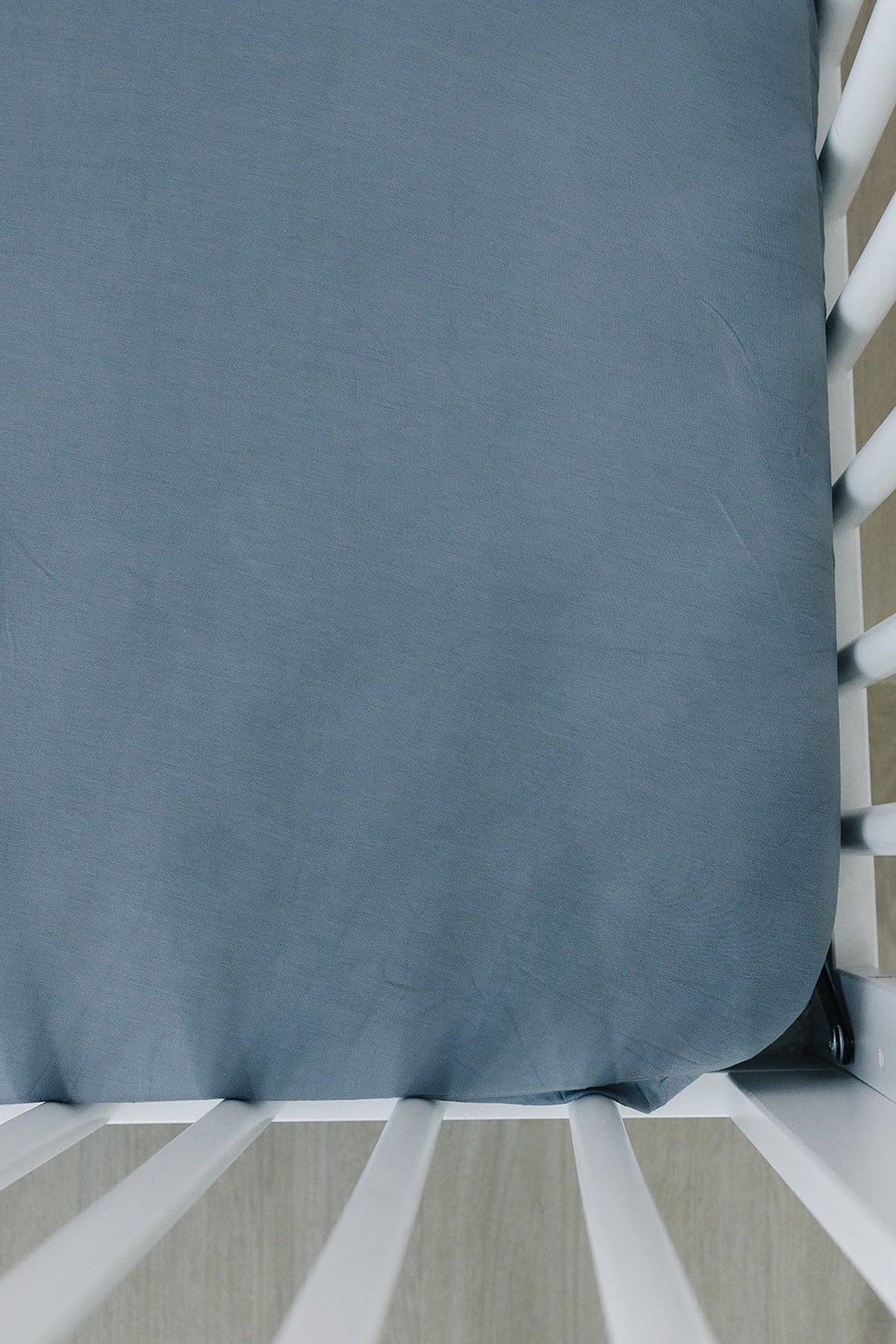 Dusty blue crib sheet made of soft bamboo fabric, fitted on a white crib.