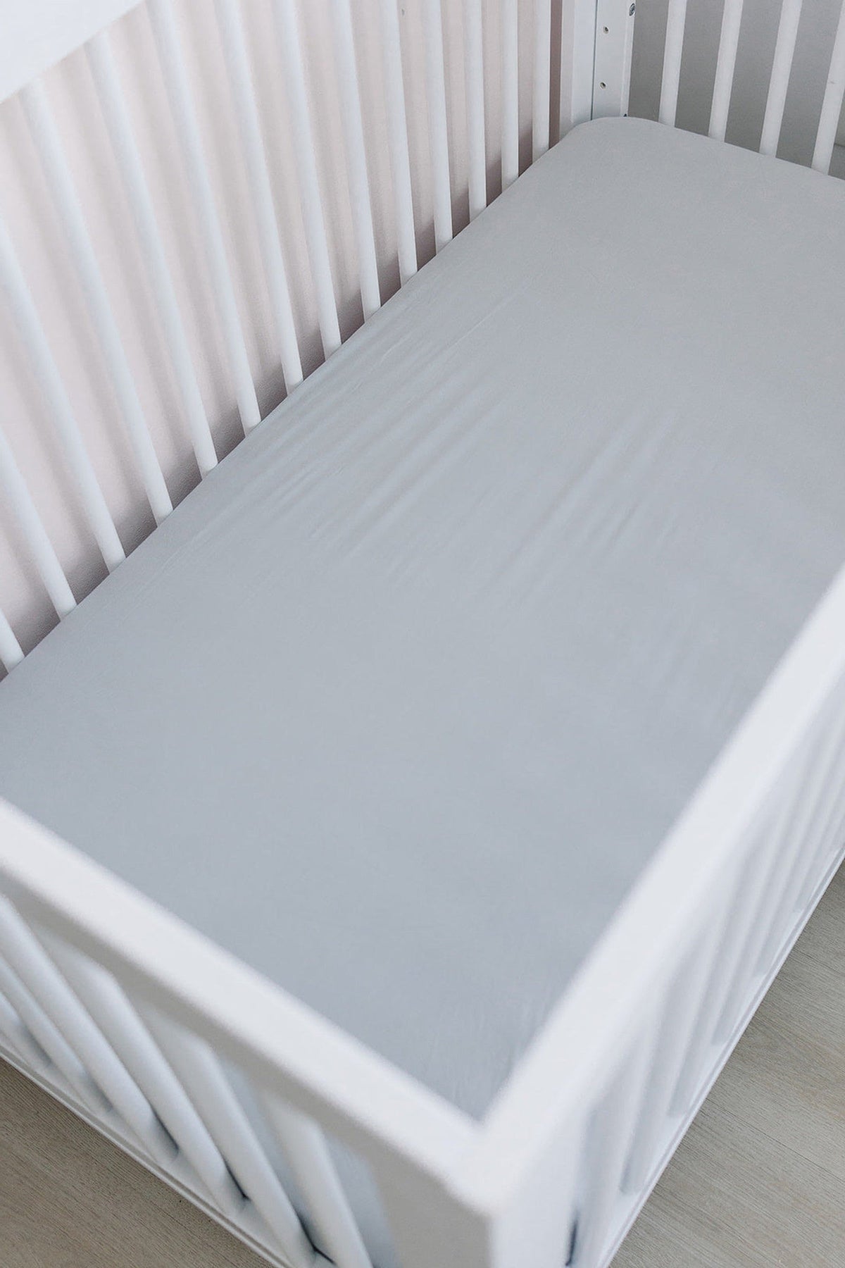 White crib with a light gray fitted sheet, showcasing a minimalist and clean nursery setting.