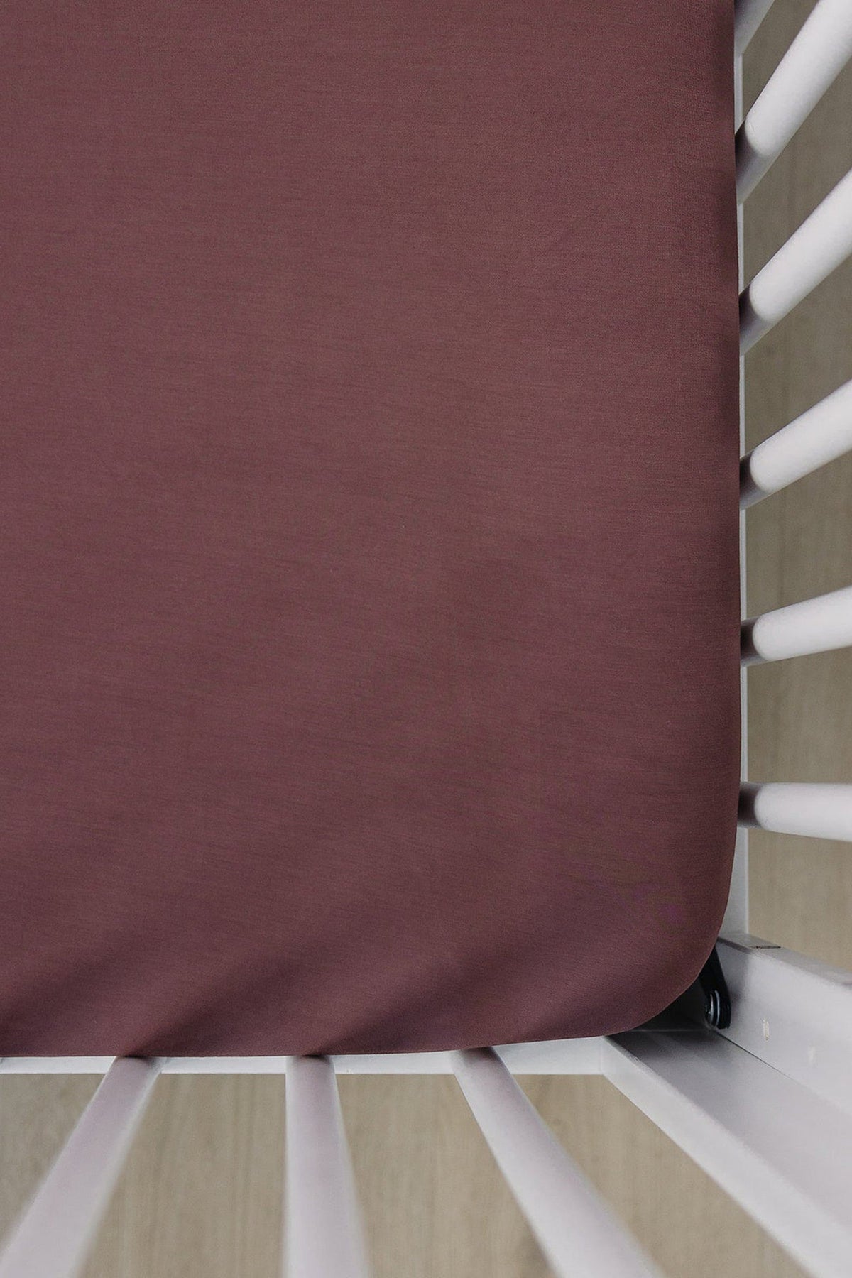 Plum-colored crib sheet on a white crib, showcasing soft bamboo fabric. Ideal for a babys nursery.