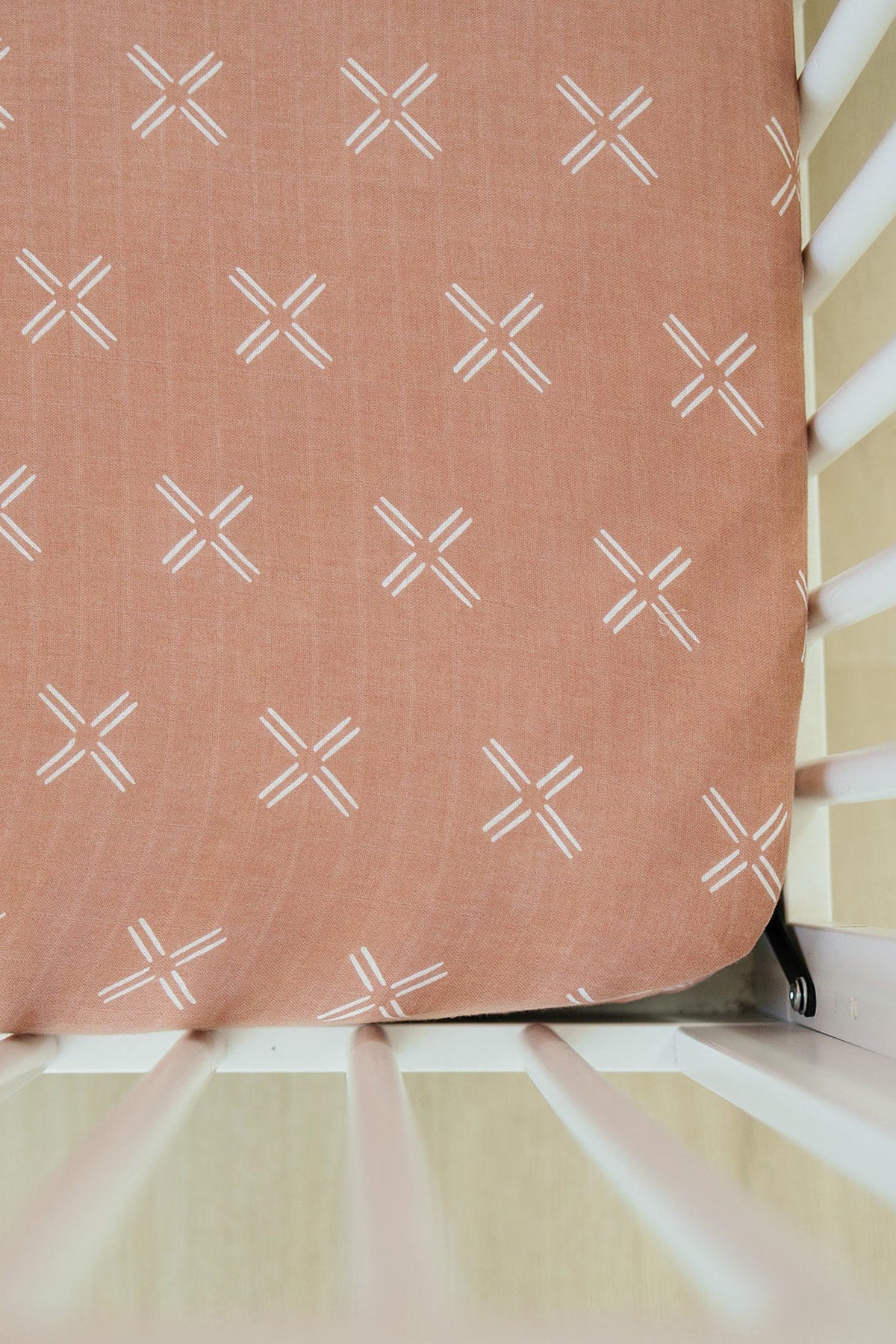 Peach-colored muslin crib sheet with white cross patterns, set on a white crib.