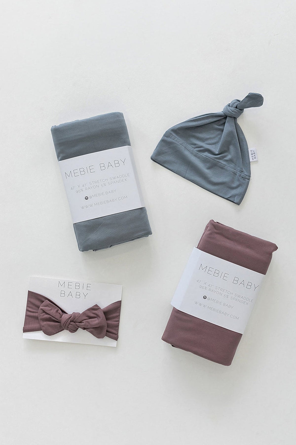 Dusty blue and mauve Mebie Baby stretch swaddle blankets with matching hat and bow on a white background.