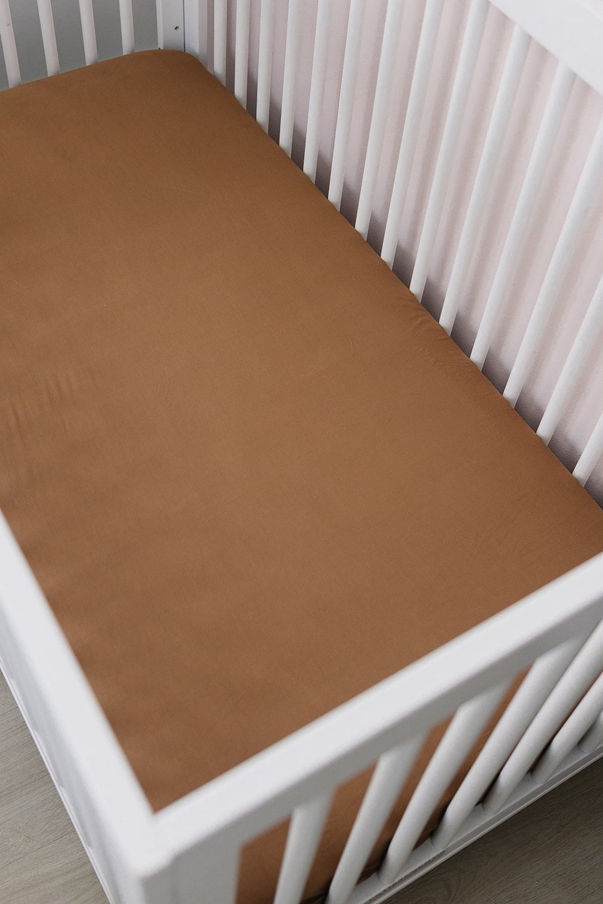 White crib with a mustard-colored bamboo stretch sheet, showcasing a minimalist and cozy nursery setting.