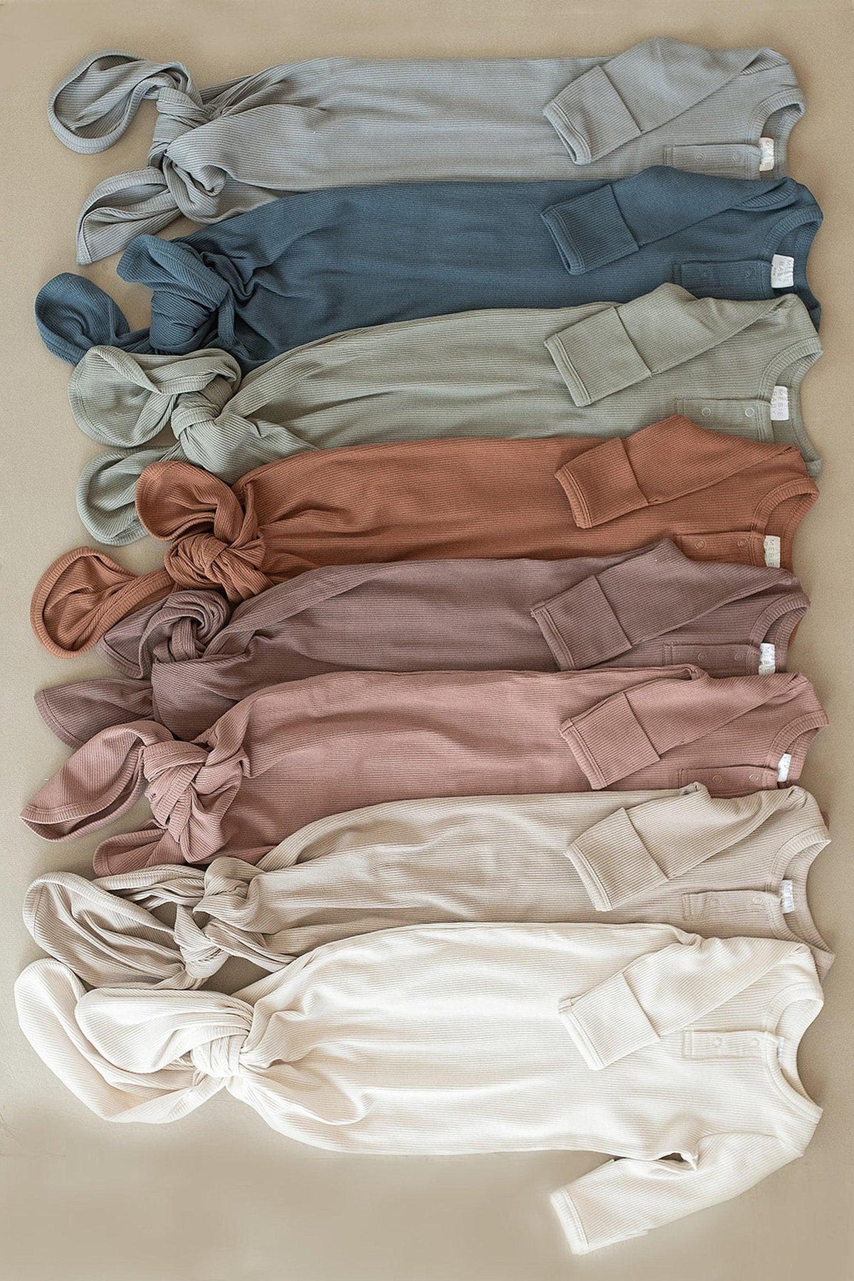 A collection of ribbed baby knot gowns in various earthy tones, laid out flat on a beige surface.
