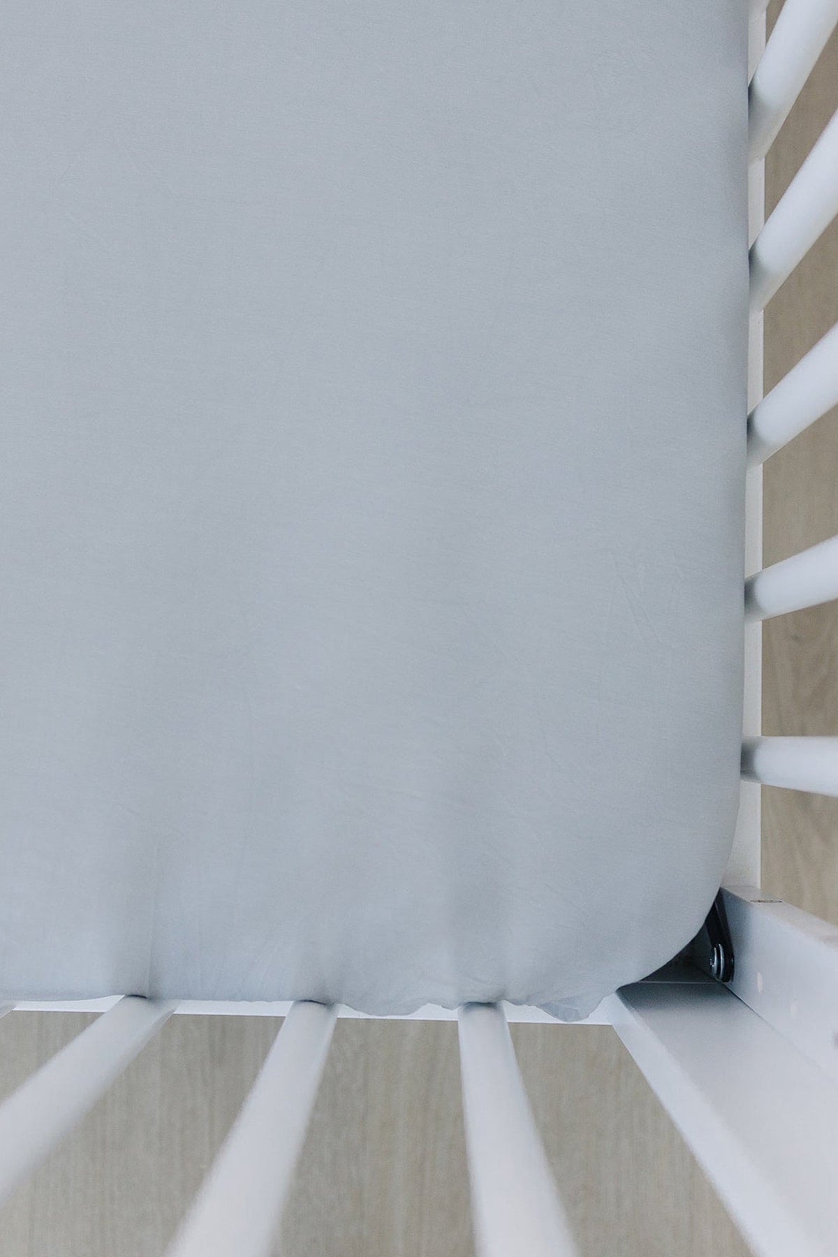 A light gray crib sheet stretched over a mattress in a white crib, showcasing a soft, smooth texture.