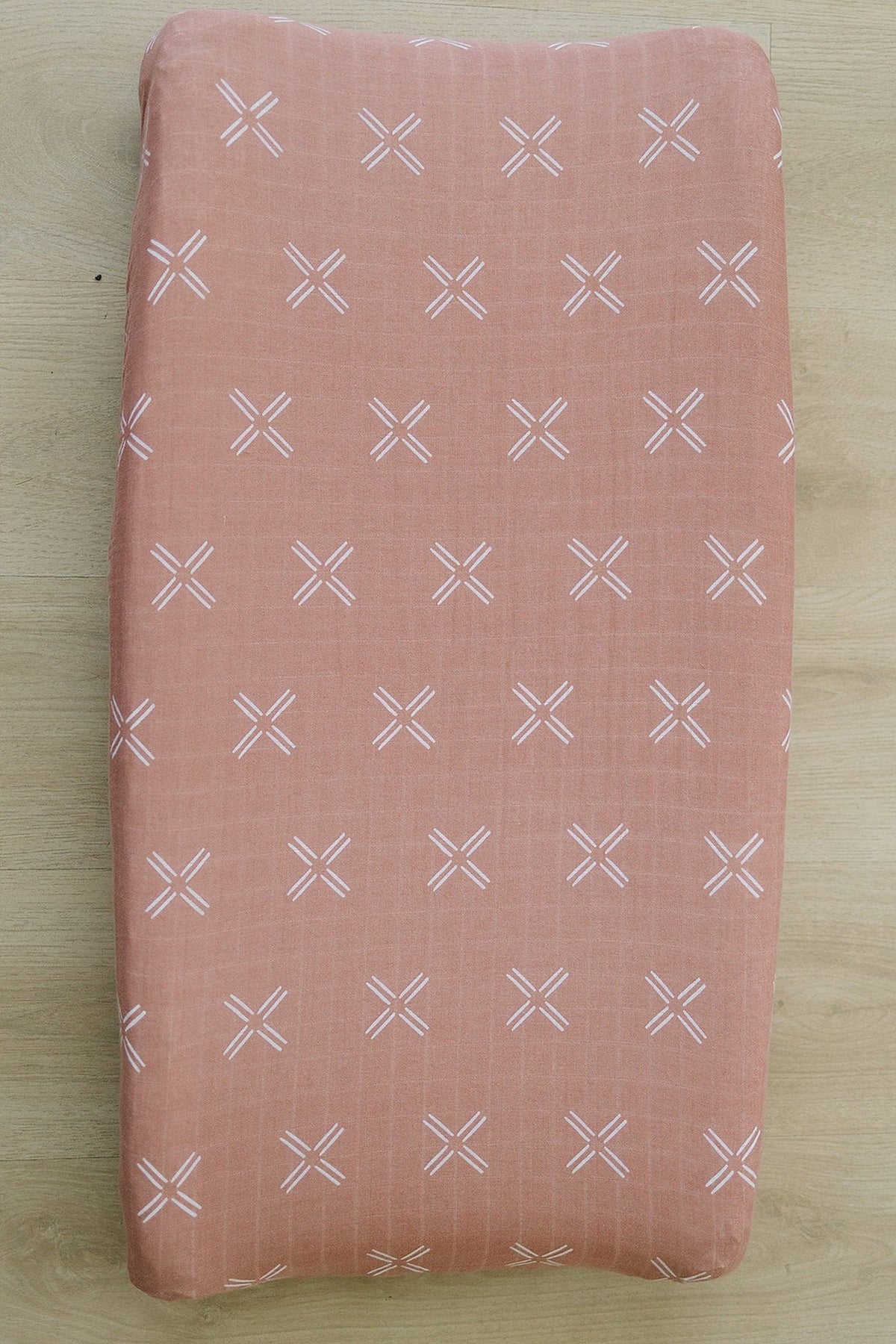 Peach muslin changing pad cover with white cross patterns on a wooden surface. Made from 100% cotton.