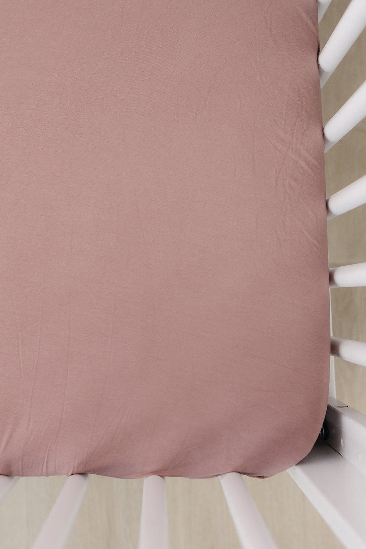 Dusty rose crib sheet made of bamboo fabric, fitted over a white crib mattress. Soft and eco-friendly.