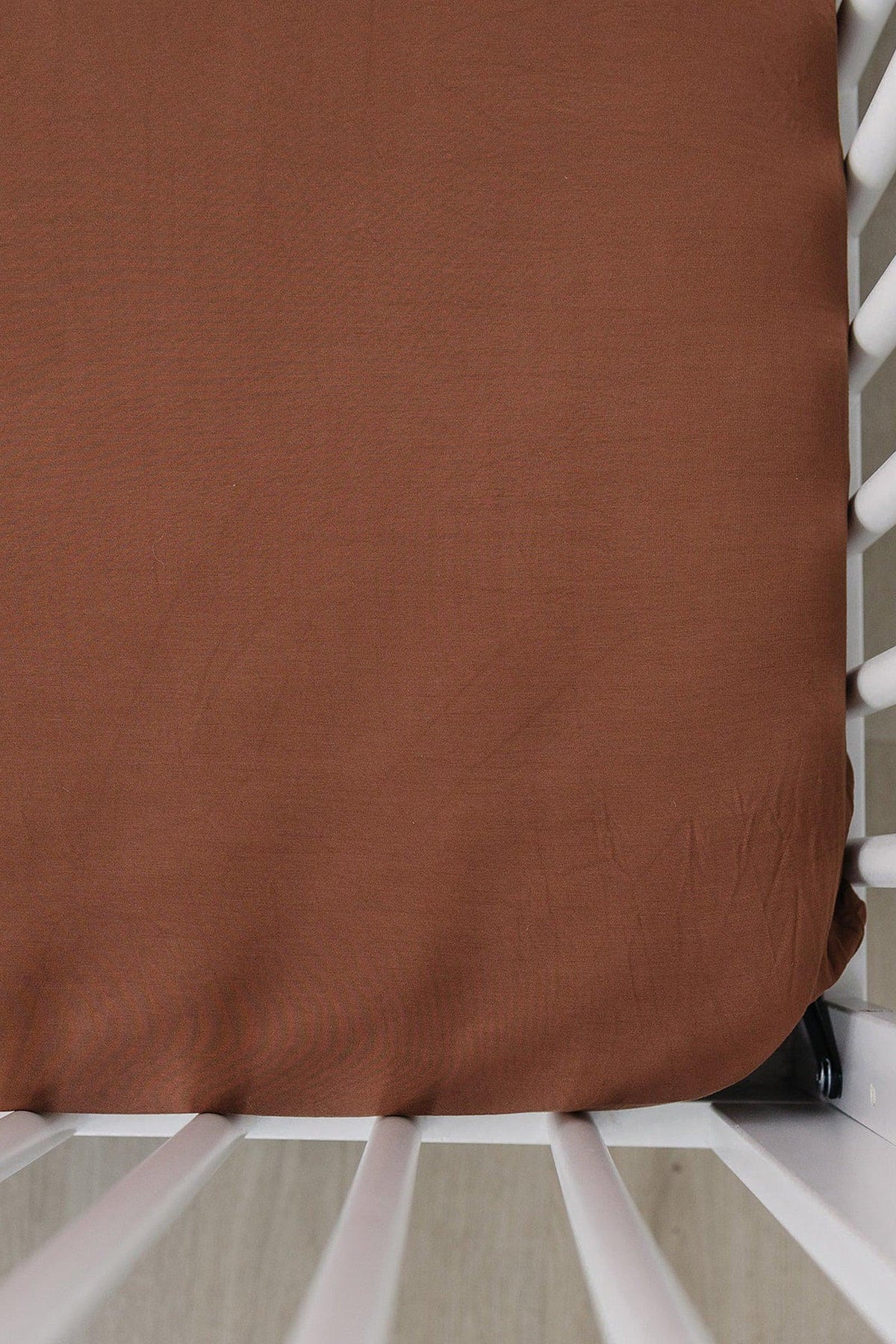 Rust-colored crib sheet made of bamboo fabric, fitted on a white crib with slatted sides.
