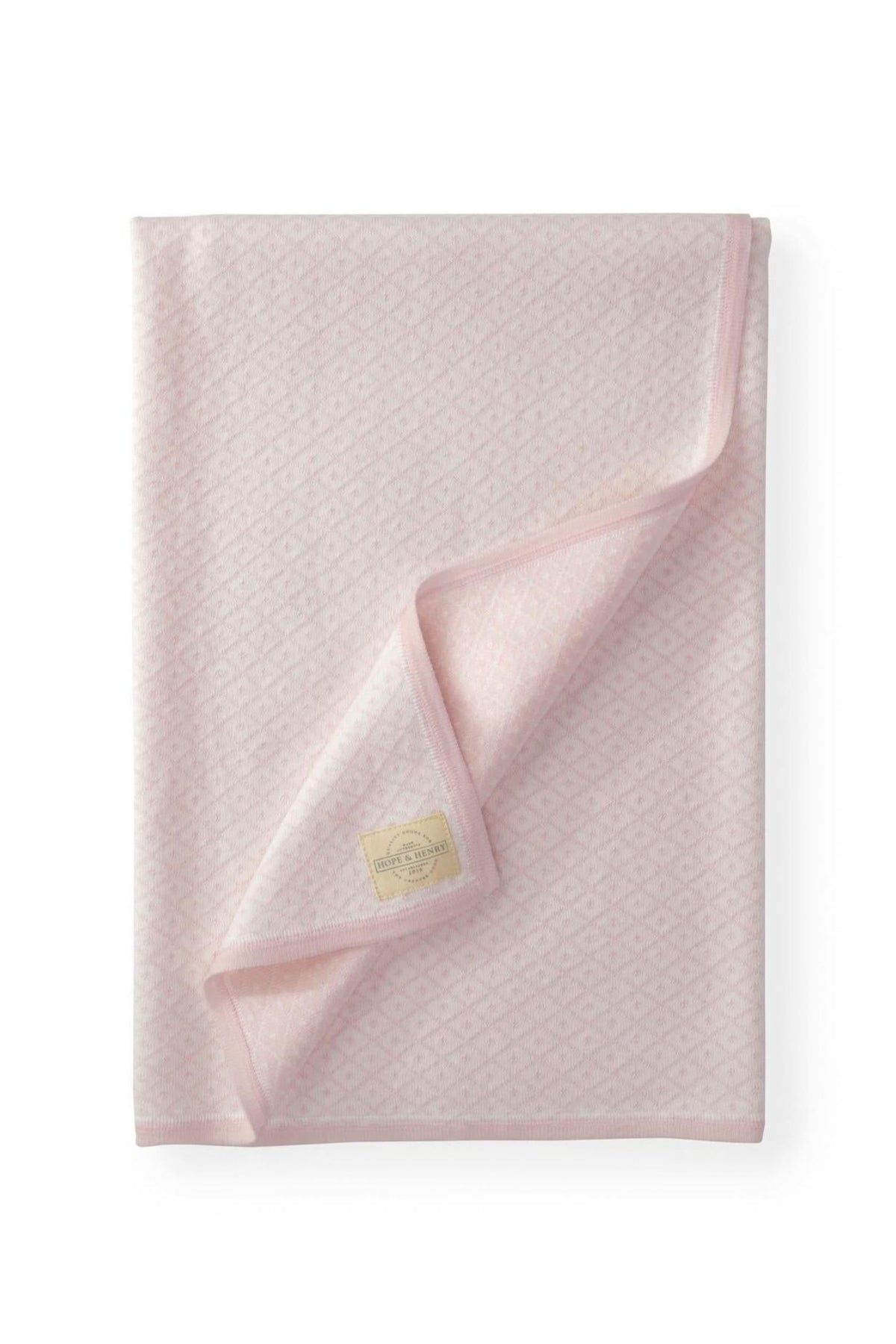 A soft pink jacquard blanket featuring an intricate diamond pattern, with a folded edge and a brand tag visible.