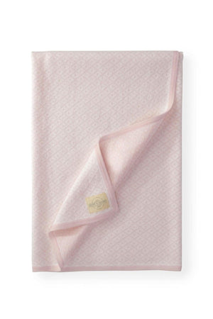 A soft pink jacquard blanket featuring an intricate diamond pattern, with a folded edge and a brand tag visible.