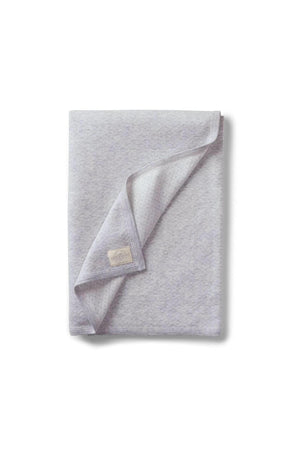 A soft gray blanket with a subtle texture, featuring a folded corner that reveals a patterned interior and a brand.