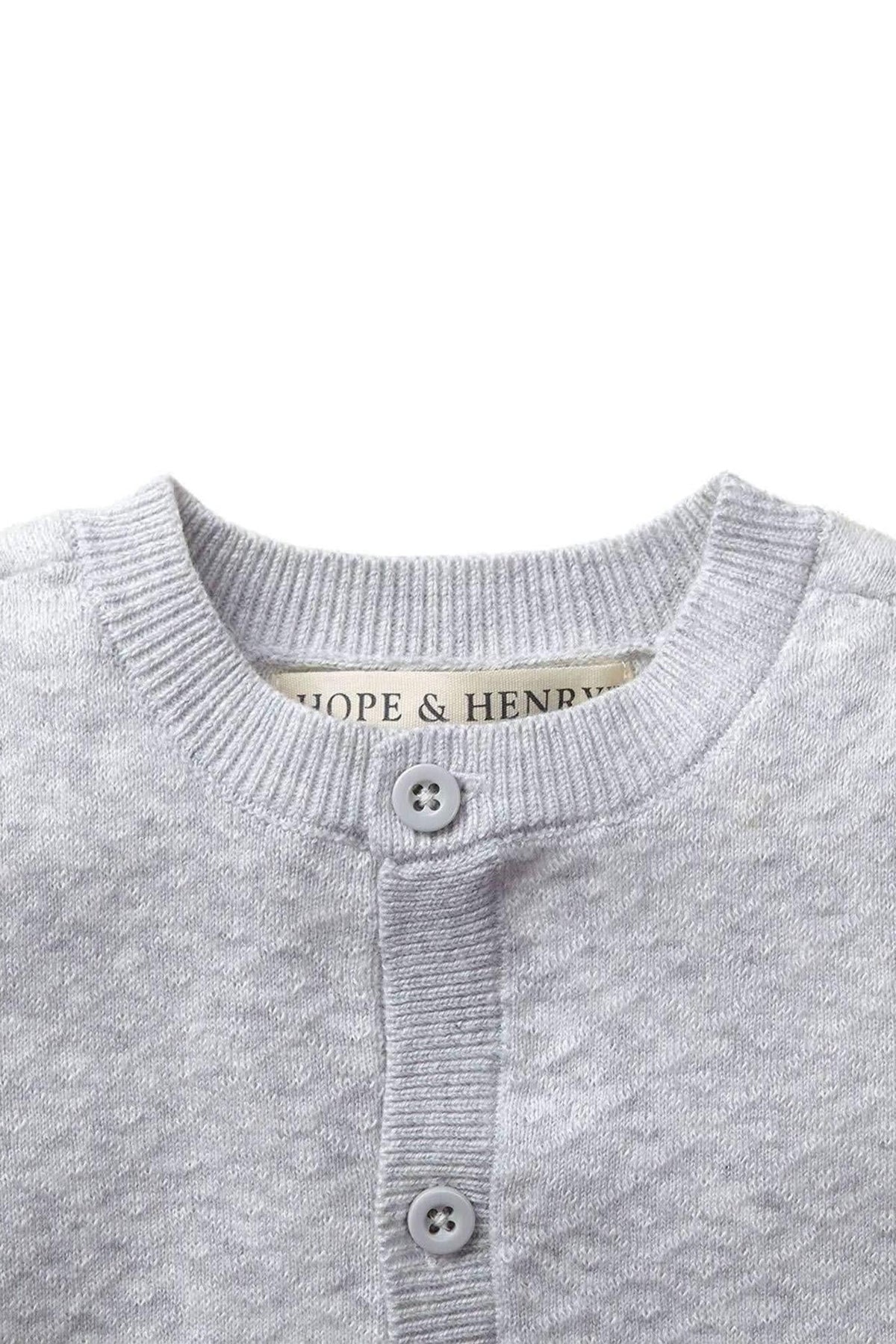 Light gray jacquard knit sweater with a diamond stitch pattern, featuring a round neckline and button closure. Made from 100% organic cotton, it’s soft and suitable for infants.