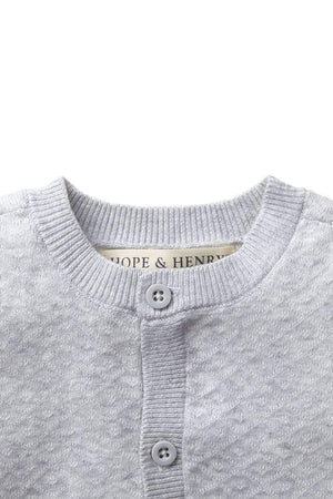 Light gray jacquard knit sweater with a diamond stitch pattern, featuring a round neckline and button closure. Made from 100% organic cotton, it’s soft and suitable for infants.