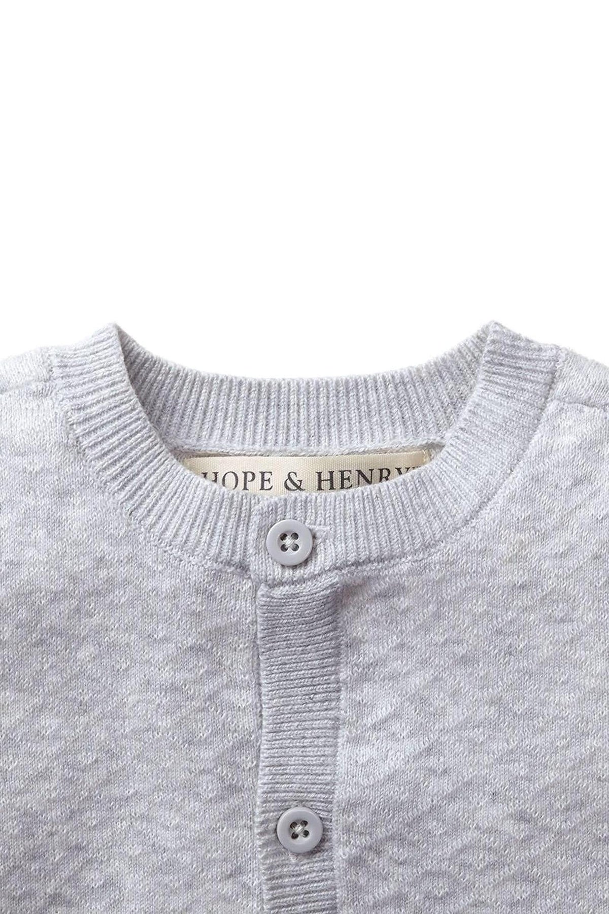 Close-up of a light gray sweater romper with a diamond pattern, featuring a button closure and Hope & Henry label.