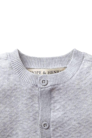 Close-up of a light gray sweater romper with a diamond pattern, featuring a button closure and Hope & Henry label.