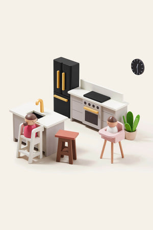 A modern kitchen playset features a black refrigerator, white cabinetry, and wooden stools. Two toy figures are positioned at a high chair and a stool, enhancing imaginative play.