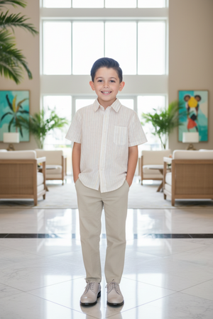 A young boy stands in a bright, modern lounge, wearing a short-sleeve striped shirt and beige trousers.