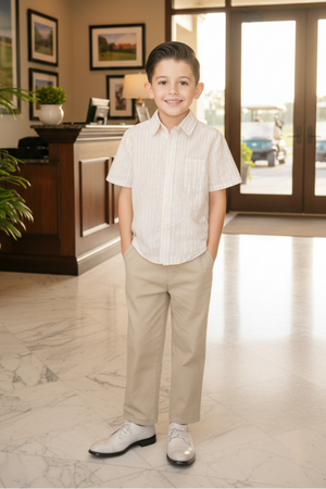 A smiling boy stands in a bright indoor setting, wearing a striped short-sleeve shirt and beige pants, with polished shoes.