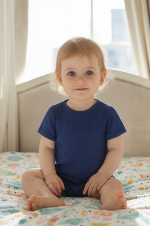 A baby sits on a colorful patterned bedspread, wearing a navy ribbed bodysuit with short sleeves and a relaxed fit.