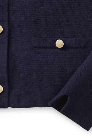 Close-up of a navy blue cardigan featuring gold buttons and a textured knit, highlighting its structured design and pocket detail.