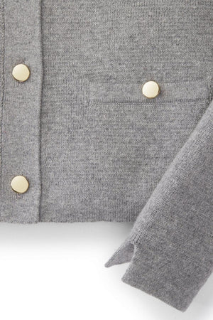 Close-up of a gray organic cotton cardigan featuring a Milano stitch, with elegant gold buttons and a small pocket, ideal for baby girls. The material appears soft.