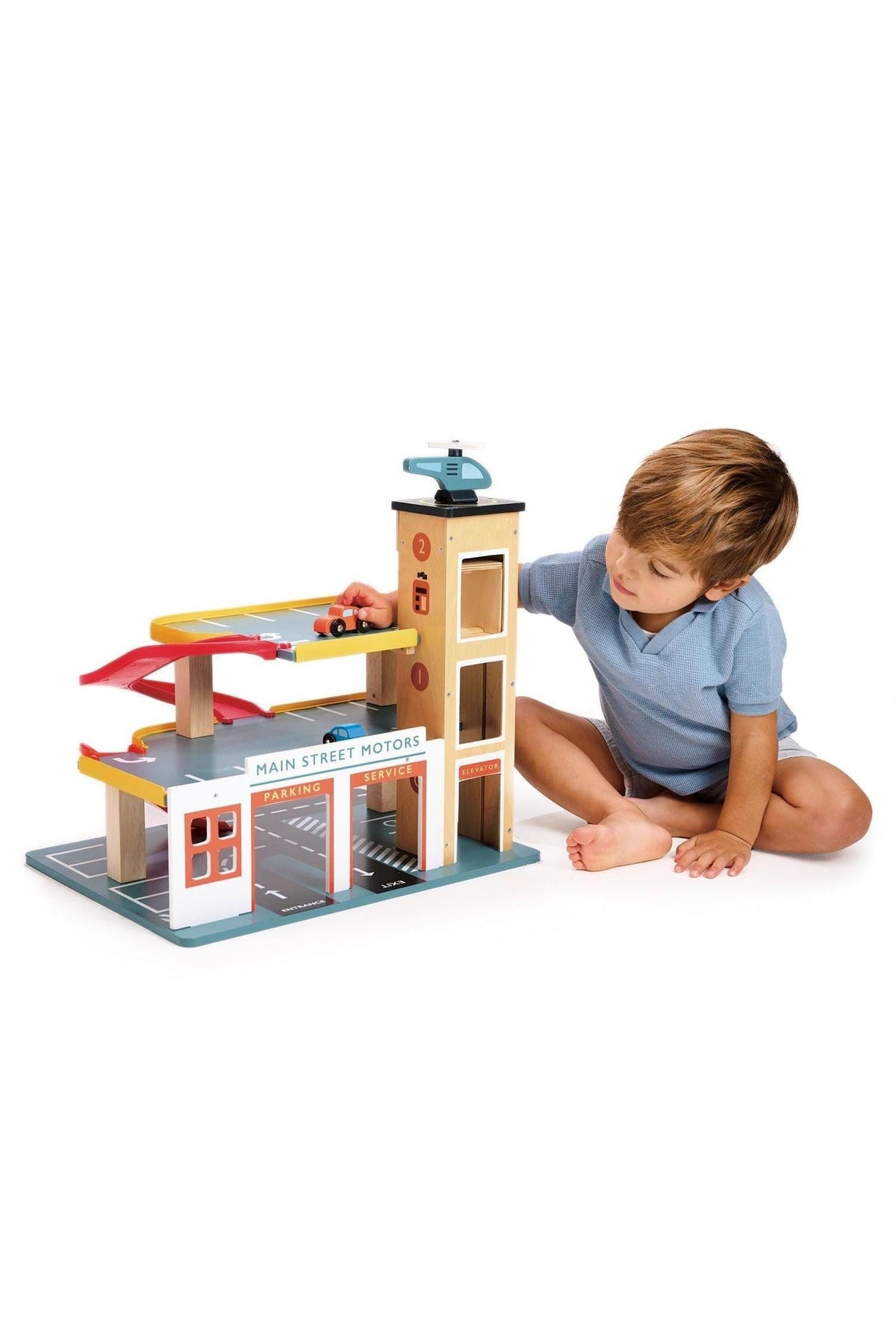 Child playing with a colorful wooden multi-level garage set, featuring ramps, a lift, and a toy helicopter.