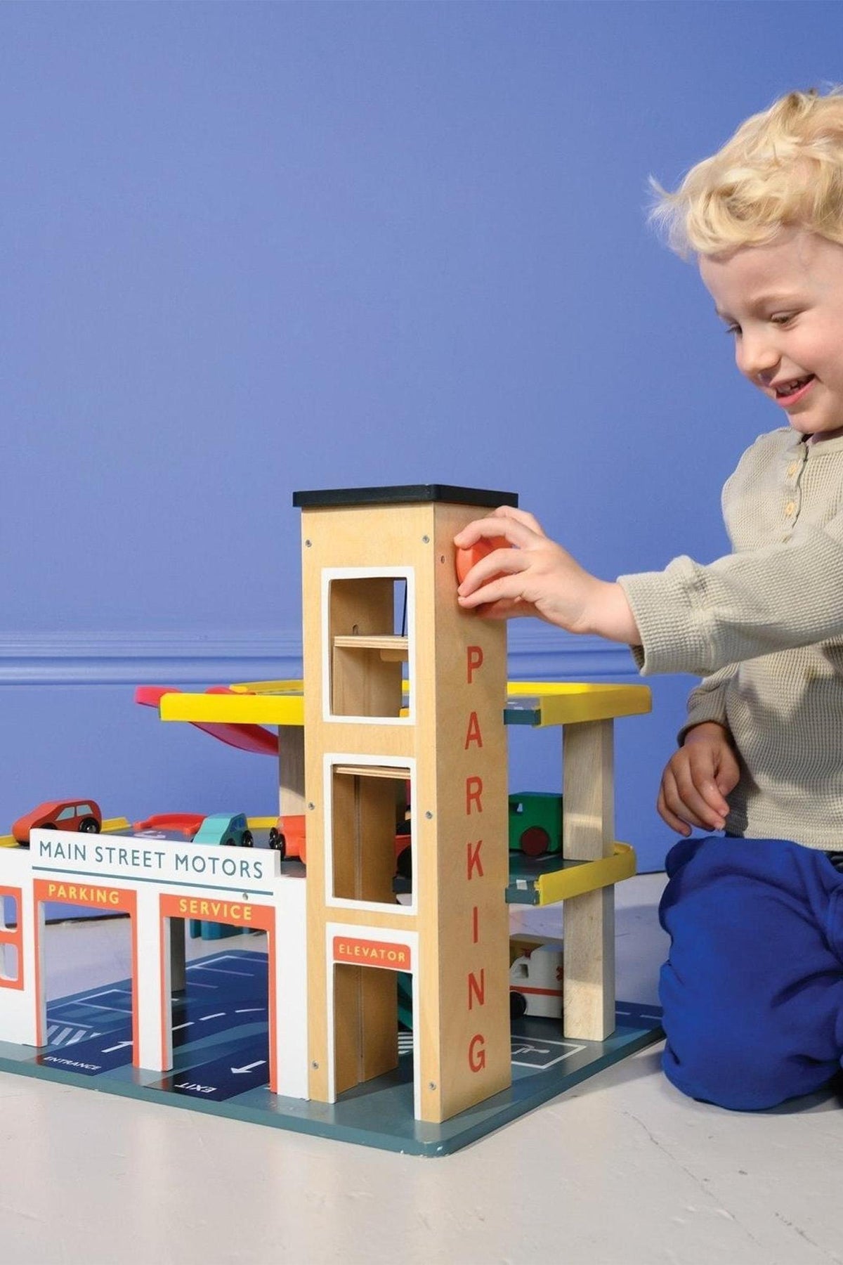 A child plays with the Mentari Wooden Toys multi-level garage, featuring colorful levels and a working lift.