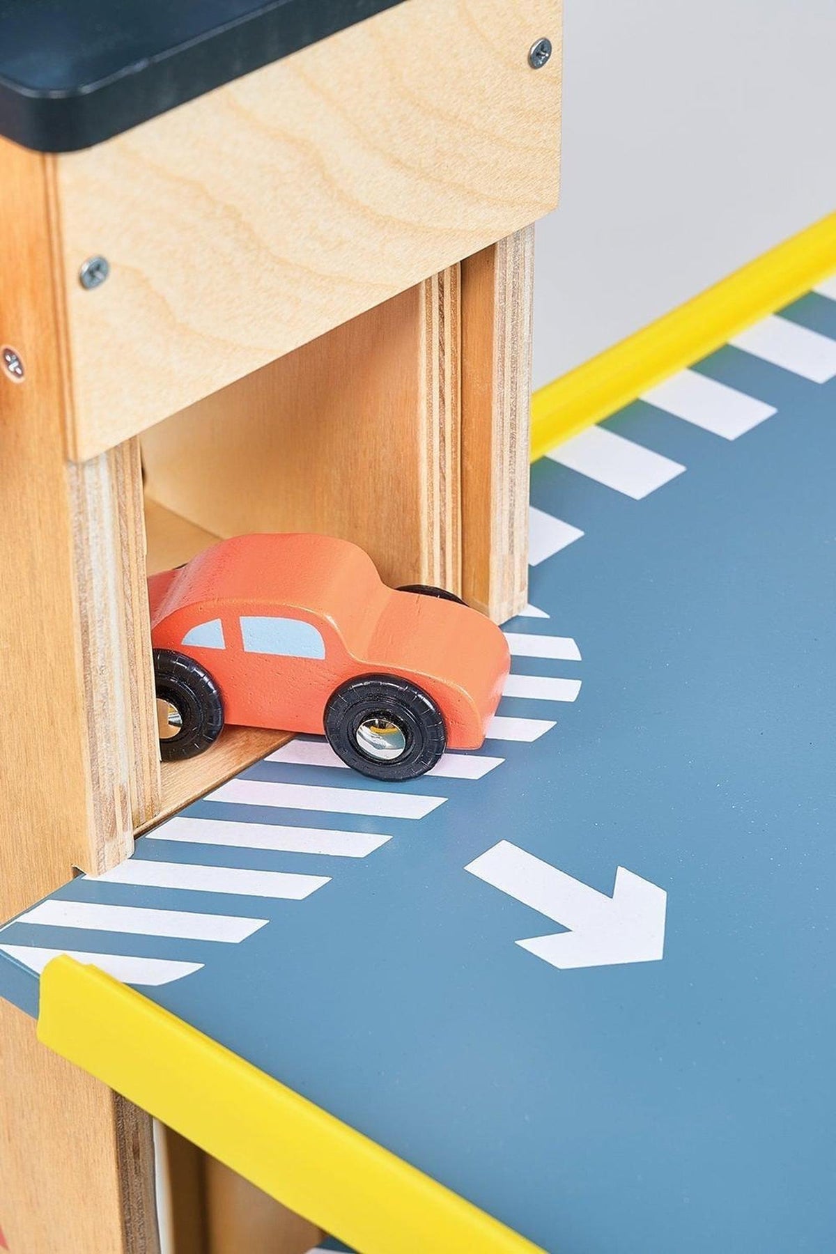 A small orange wooden toy car on a blue and white striped ramp with a yellow edge.