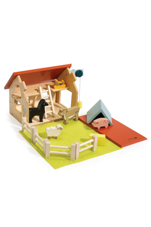 A colorful wooden farm playset features a barn, animal figures, and a fenced area on a green mat. This eco-friendly toy encourages imaginative play for young children.