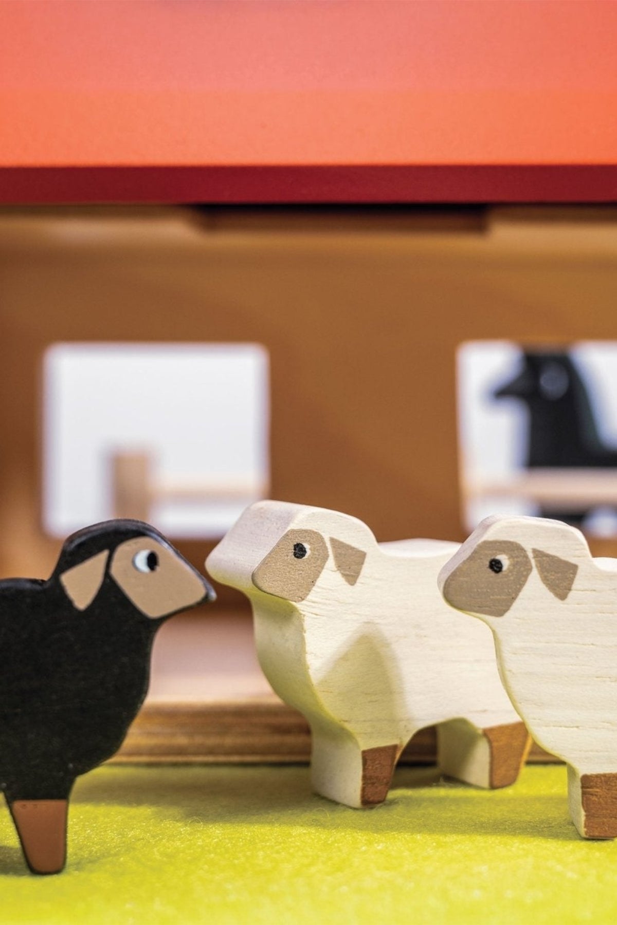 Wooden sheep figures in front of a small wooden house model.